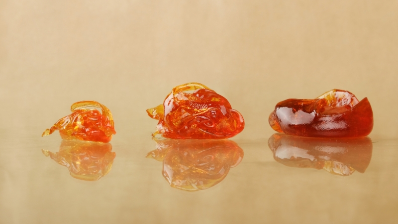 Three pieces of amber-colored cannabis concentrate lined up on a reflective surface, showing different types of dabs
