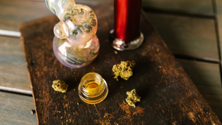 Glass pipe, cannabis buds, dab concentrate, and torch on a wooden surface, showing tools used to explain what is dabbing